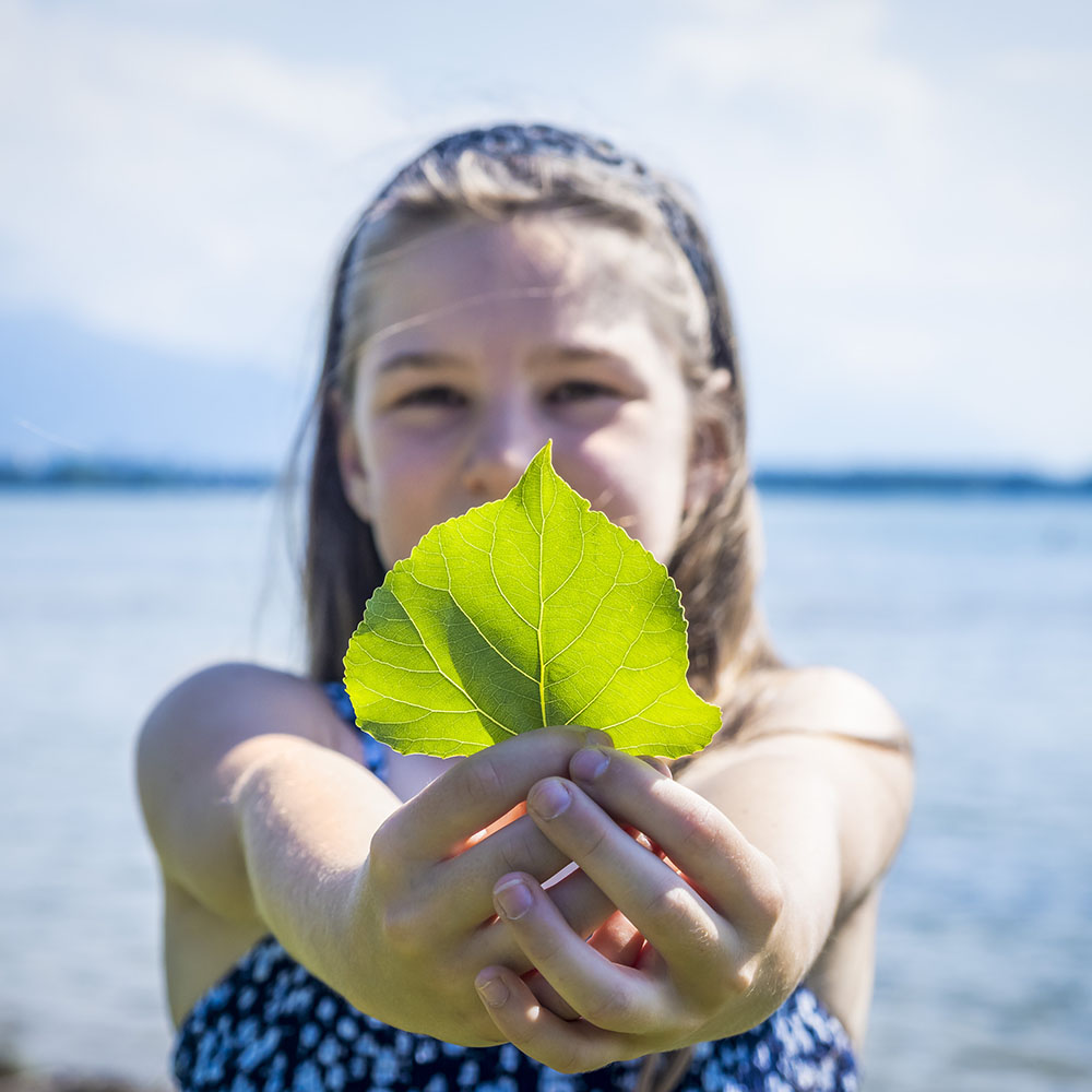 Ein Mädchen hält ein Blatt in den Händen, um Nachhaltigkeit zu symbolisieren.